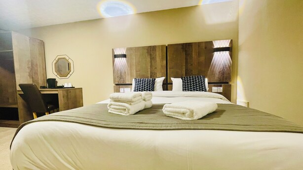 A hotel room with a large bed, a desk, and a chair. There are two lamps on the wall and a mirror above the desk. - Hylands Hotel (Coventry)