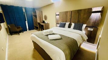 Quarto de hotel com cama grande, escrivaninha, cadeira e guarda-roupa.