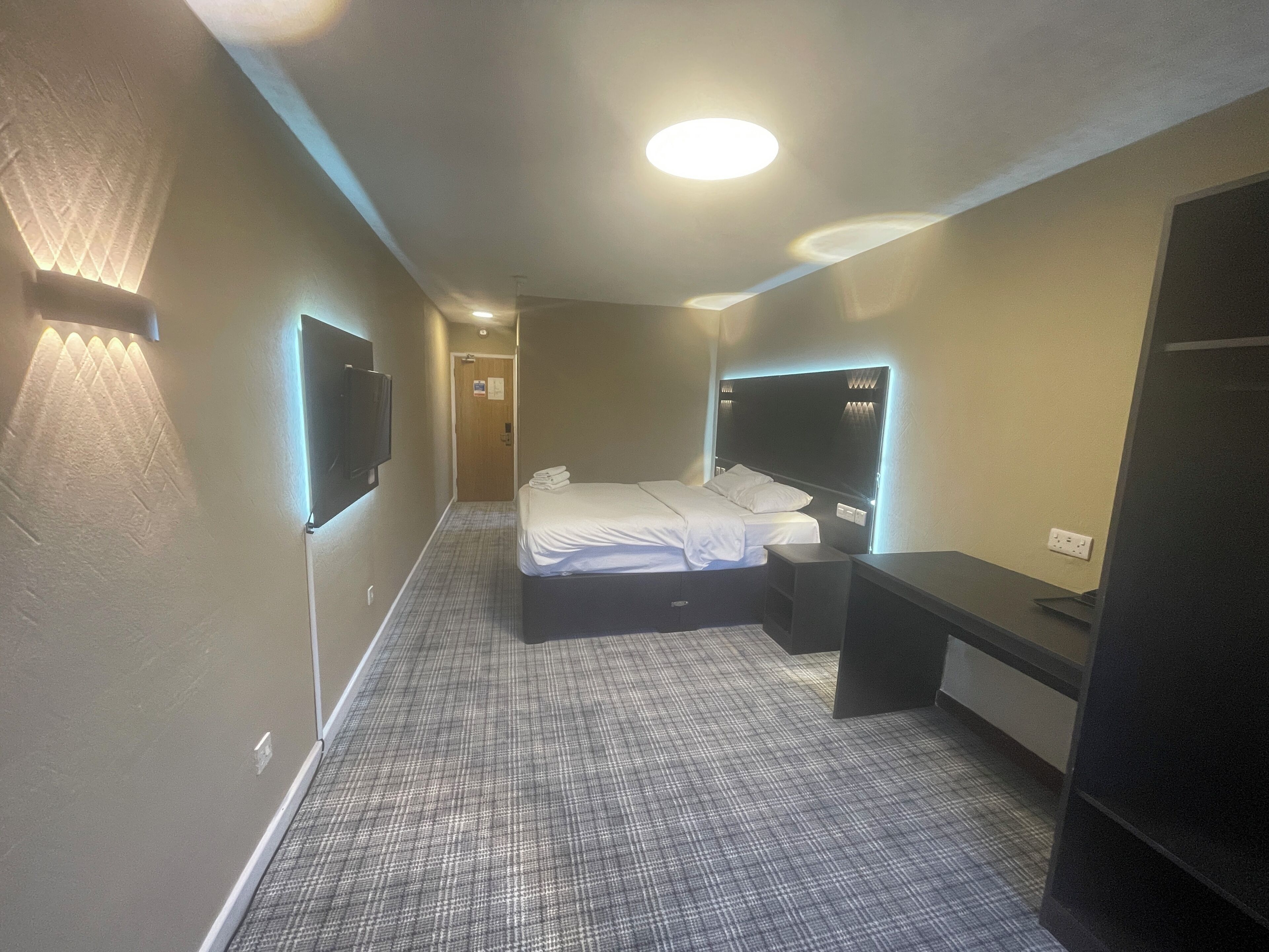 A hotel room with a bed, bedside tables, a desk, and a TV mounted on the wall.