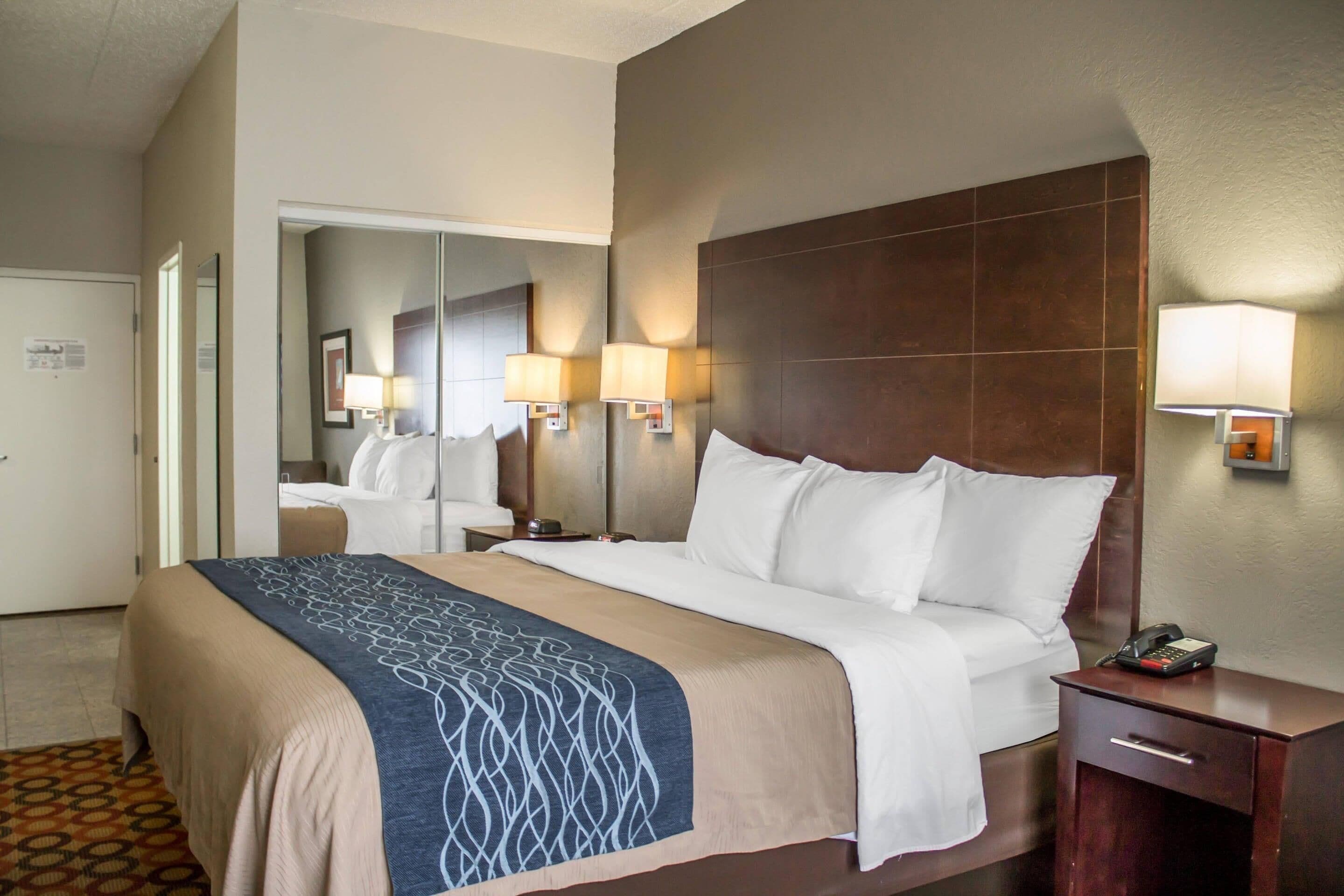 A hotel room with a large bed, bedside lamps, a nightstand, and a mirror.