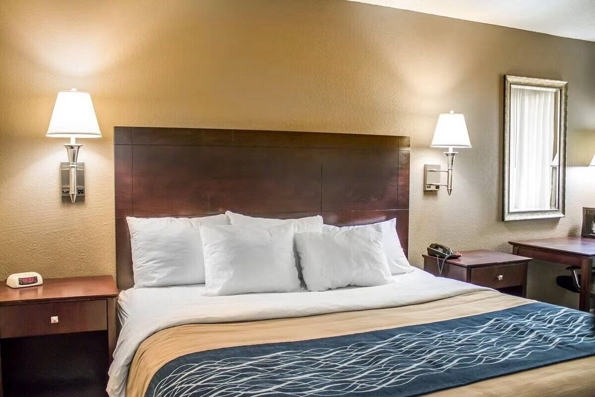 A hotel room with a large bed, two bedside lamps, a nightstand with a phone, and a window with curtains.
