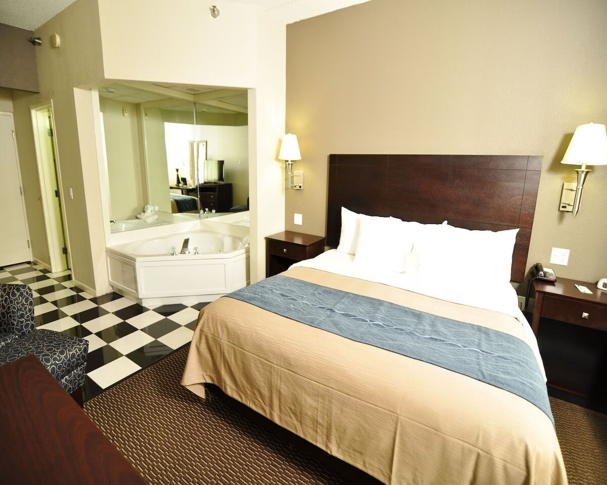 Camera d'albergo con un ampio letto, bagno separato con vasca, una poltrona e un comodino con lampada.