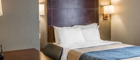 A hotel room with a large bed, a wooden nightstand, and two wall-mounted lamps.