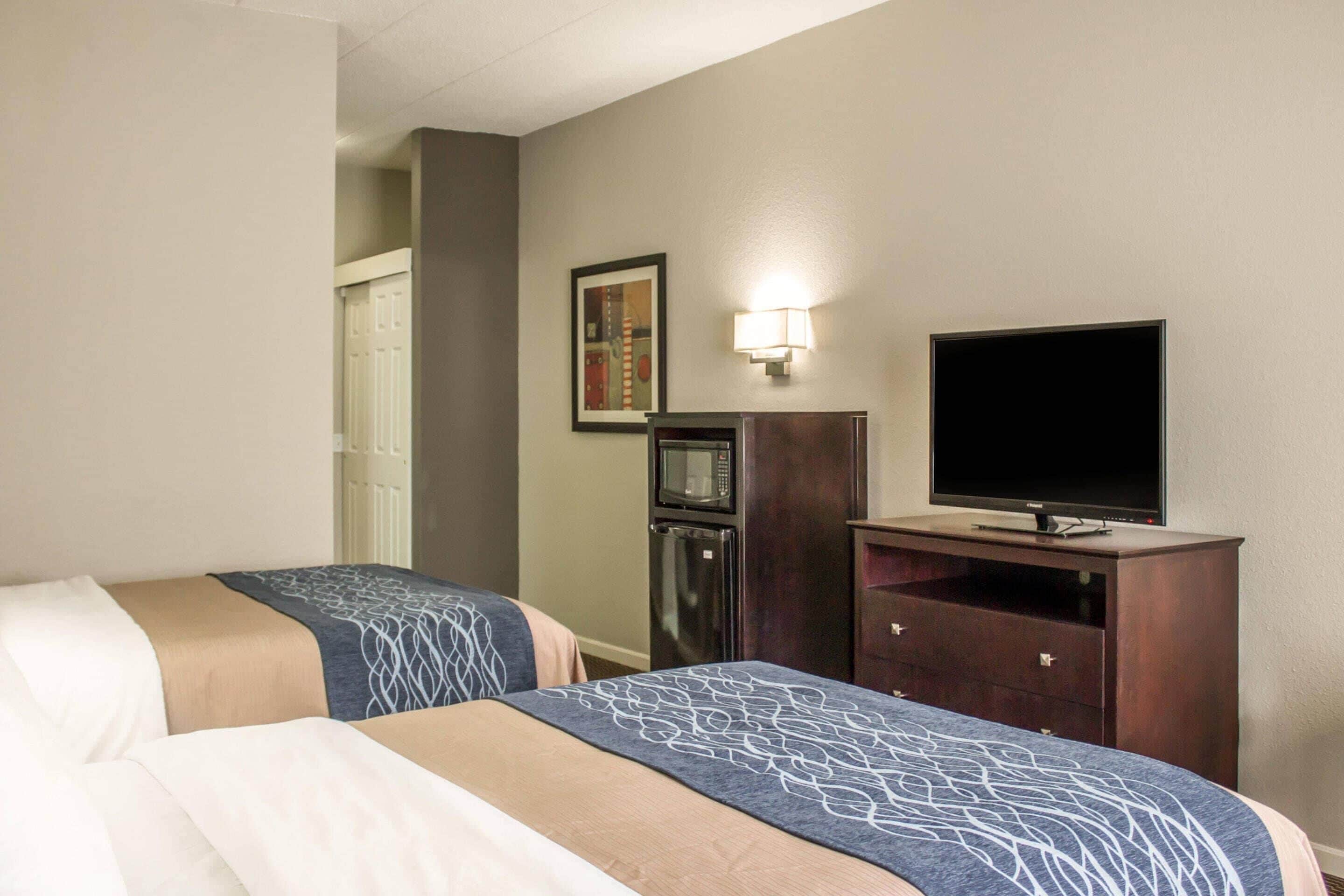 A hotel room with two beds, a TV, a microwave, and a refrigerator.