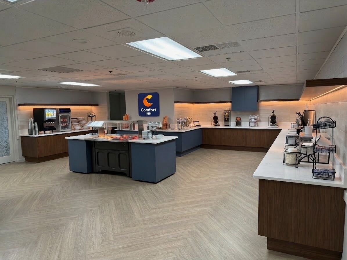 A hotel lobby with a central reception desk, a Comfort Inn sign, and a counter with various items.