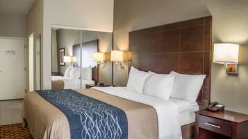 Habitación de hotel con una cama grande, una mesita de noche con lámpara, un espejo y un teléfono.
