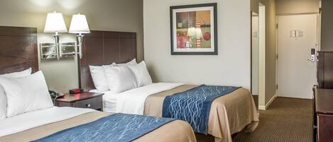 A hotel room with two beds, a nightstand, a lamp, a framed picture, and a door.