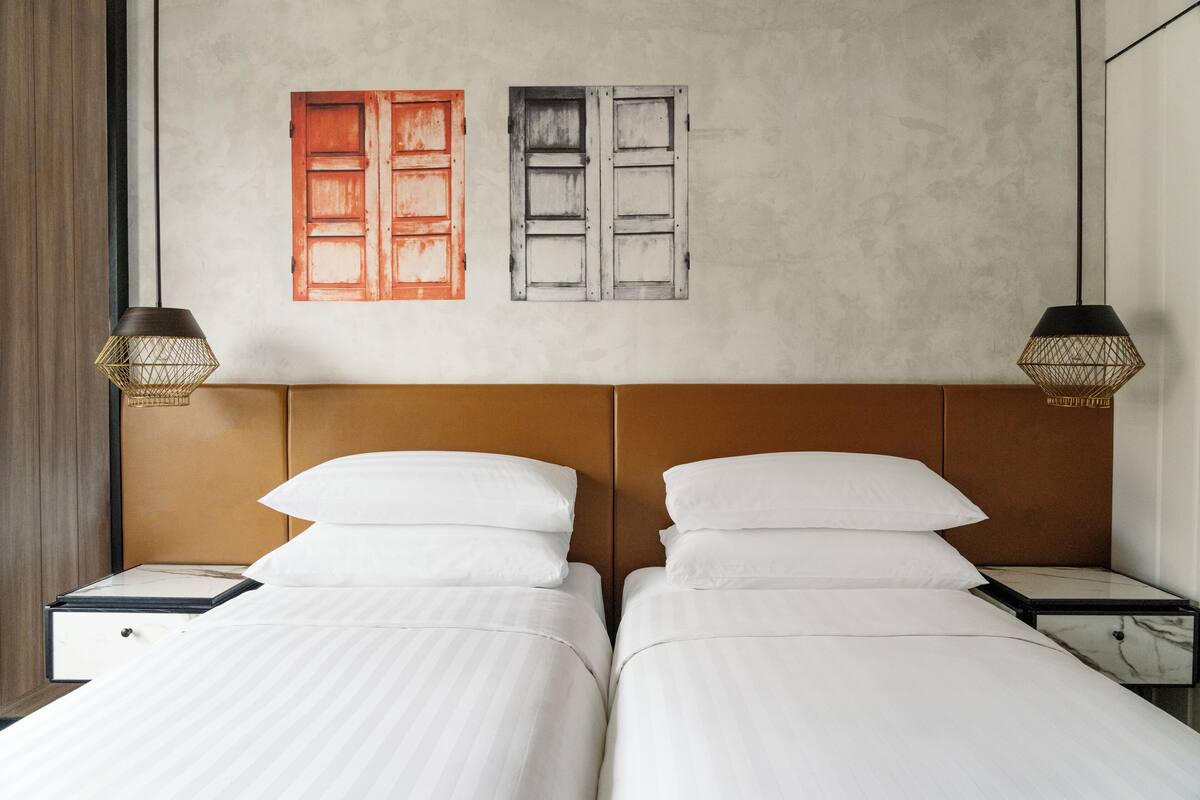 A hotel room with two beds, a wooden headboard, and two bedside lamps.