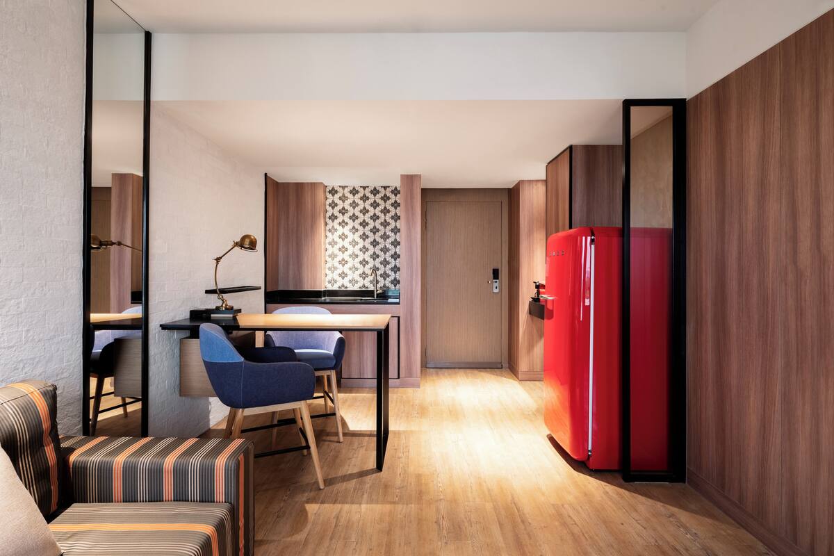 A compact living space with a kitchenette, a dining area with a blue chair, and a red refrigerator.