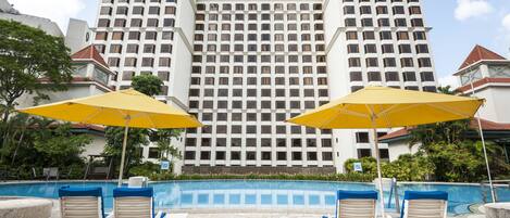 Un hôtel doté d’une grande piscine, de parasols jaunes et de chaises longues.