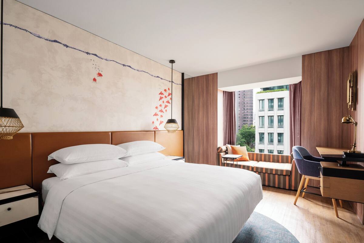 A modern hotel room with a large bed, a desk, and a view of the cityscape.