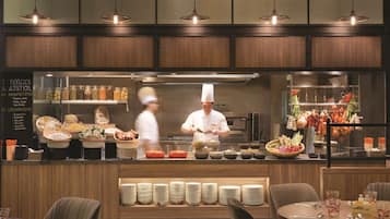 A restaurant with a buffet counter, a chef preparing food, and a variety of dishes displayed.