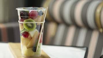 A clear glass with various fruits and a straw on a wooden board.