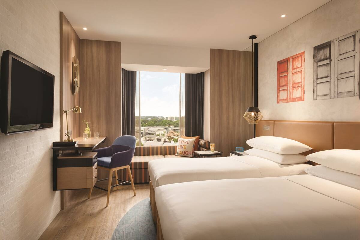 A hotel room with a large bed, a desk, a chair, a TV, and a window with a city view.