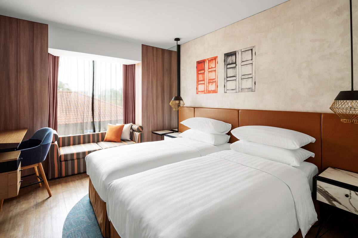 A hotel room with two beds, a desk, and a window with curtains.