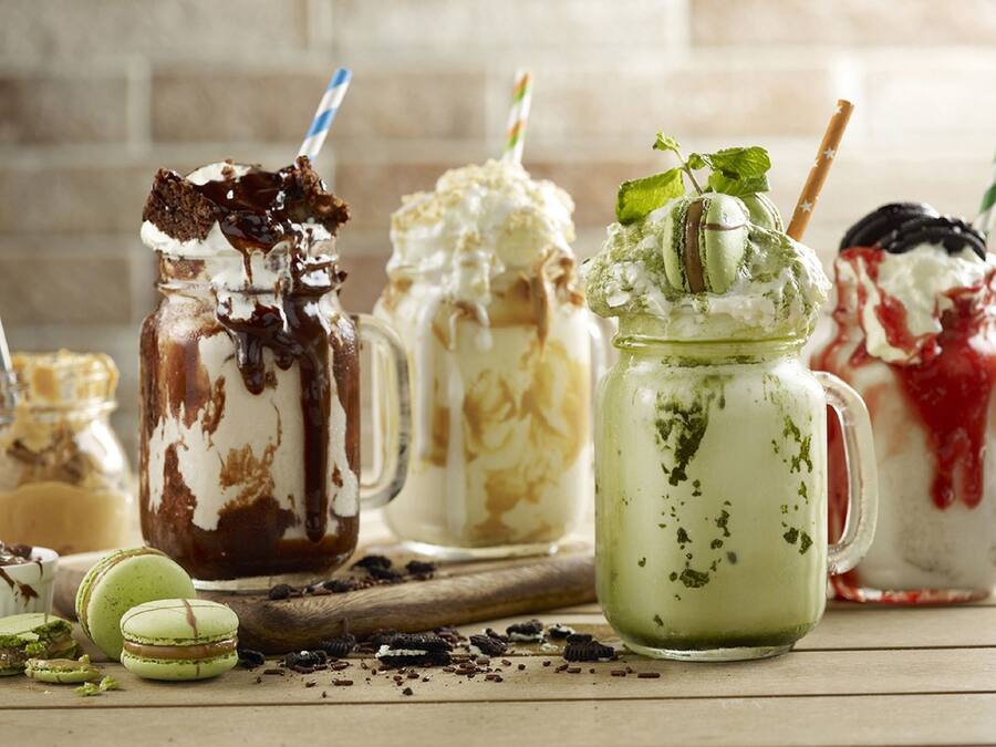 Diverse desserts in verschillende bakjes, waaronder een groene matcha-drank, een chocoladedessert met slagroom, en een rode dessert met slagroom.