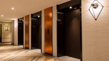 A hotel lobby with a modern design, featuring a geometric patterned floor, a wall-mounted light fixture, and a series of elevators.