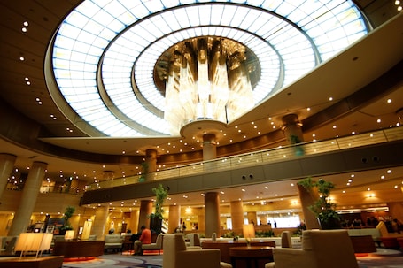 A spacious lobby with a large central chandelier, multiple seating areas, and a high ceiling with a skylight.