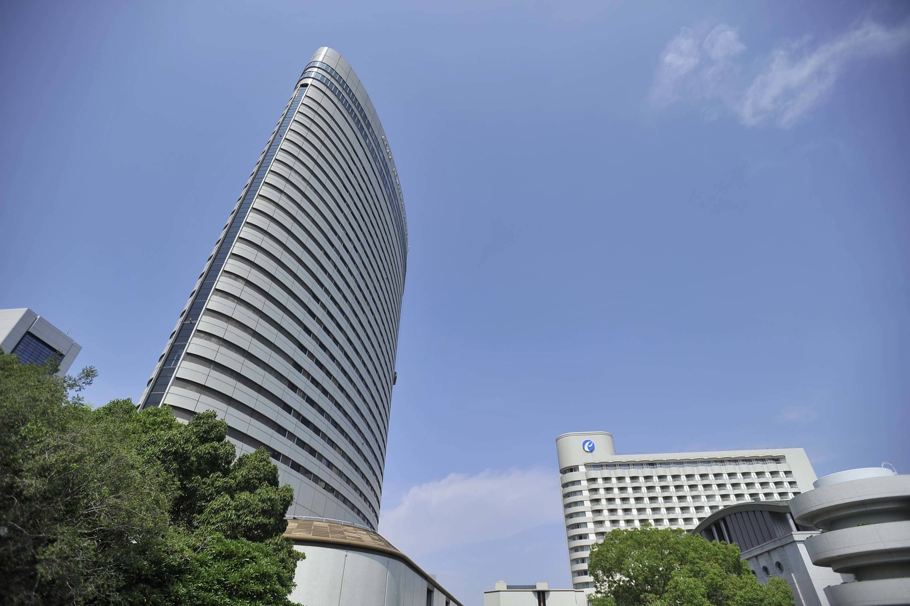 A tall, curved skyscraper with a modern design, surrounded by other buildings and trees.