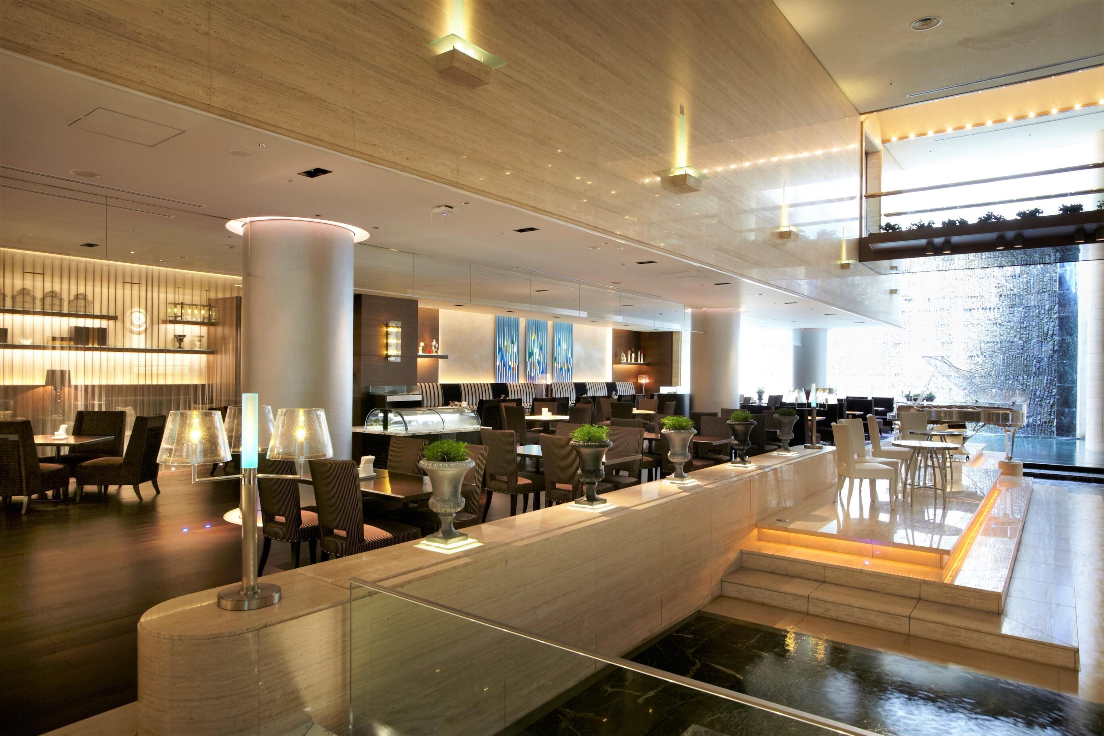 A modern hotel lobby with a reception desk, seating area, and a view of a waterfall.