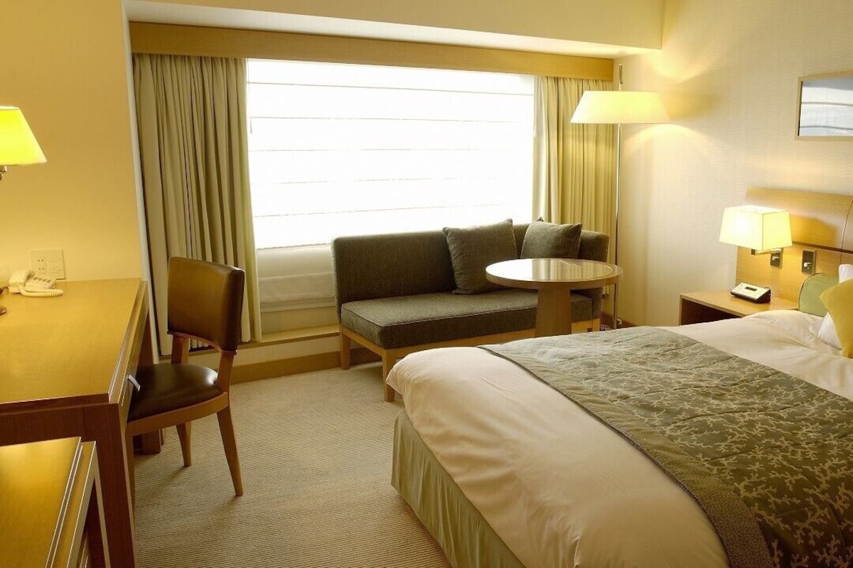 A hotel room with a bed, a sofa, a small table, a desk, and a nightstand.