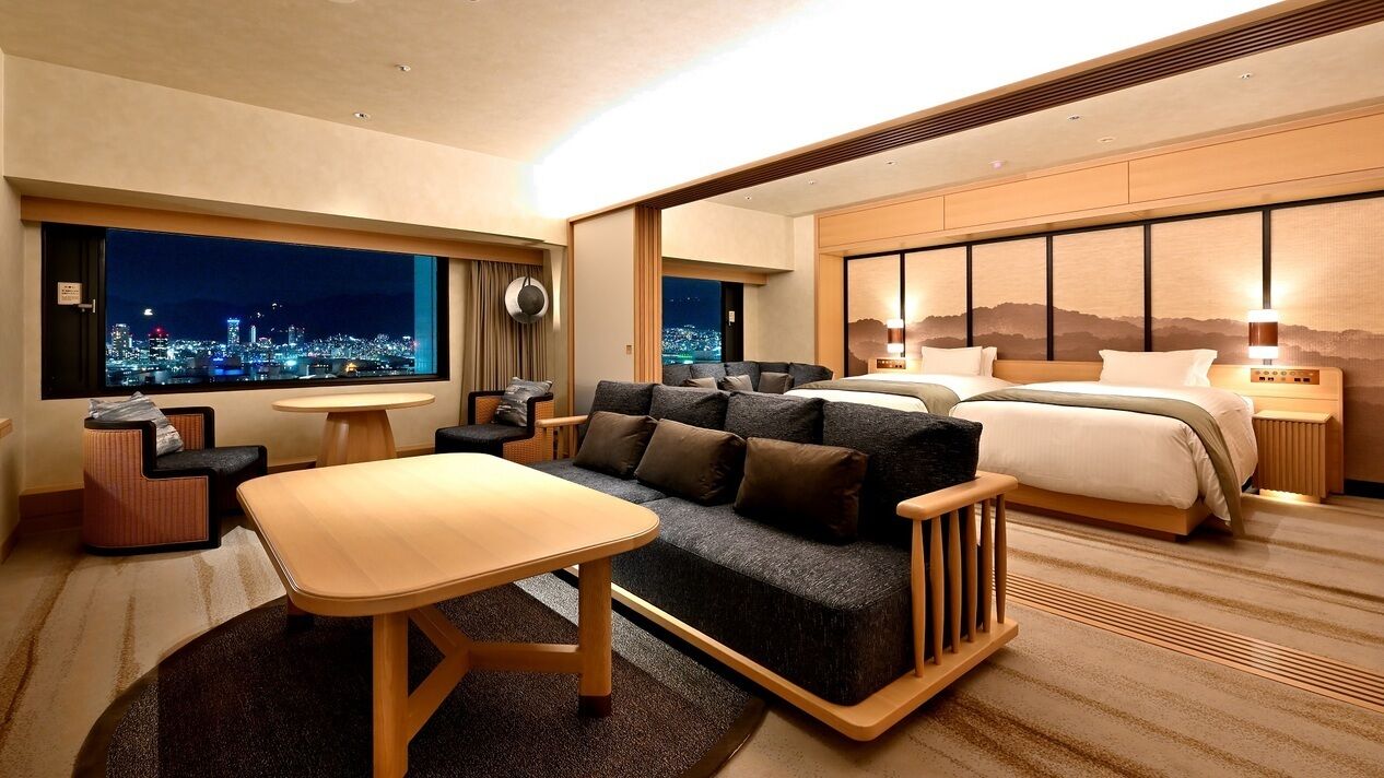 Camera d'albergo con divano, letto, tavolo da pranzo e vista sulla città illuminata di notte.