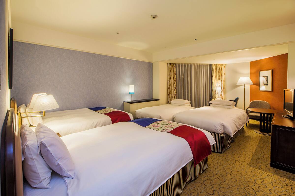 A hotel room with four beds, a desk, a chair, and a television.
