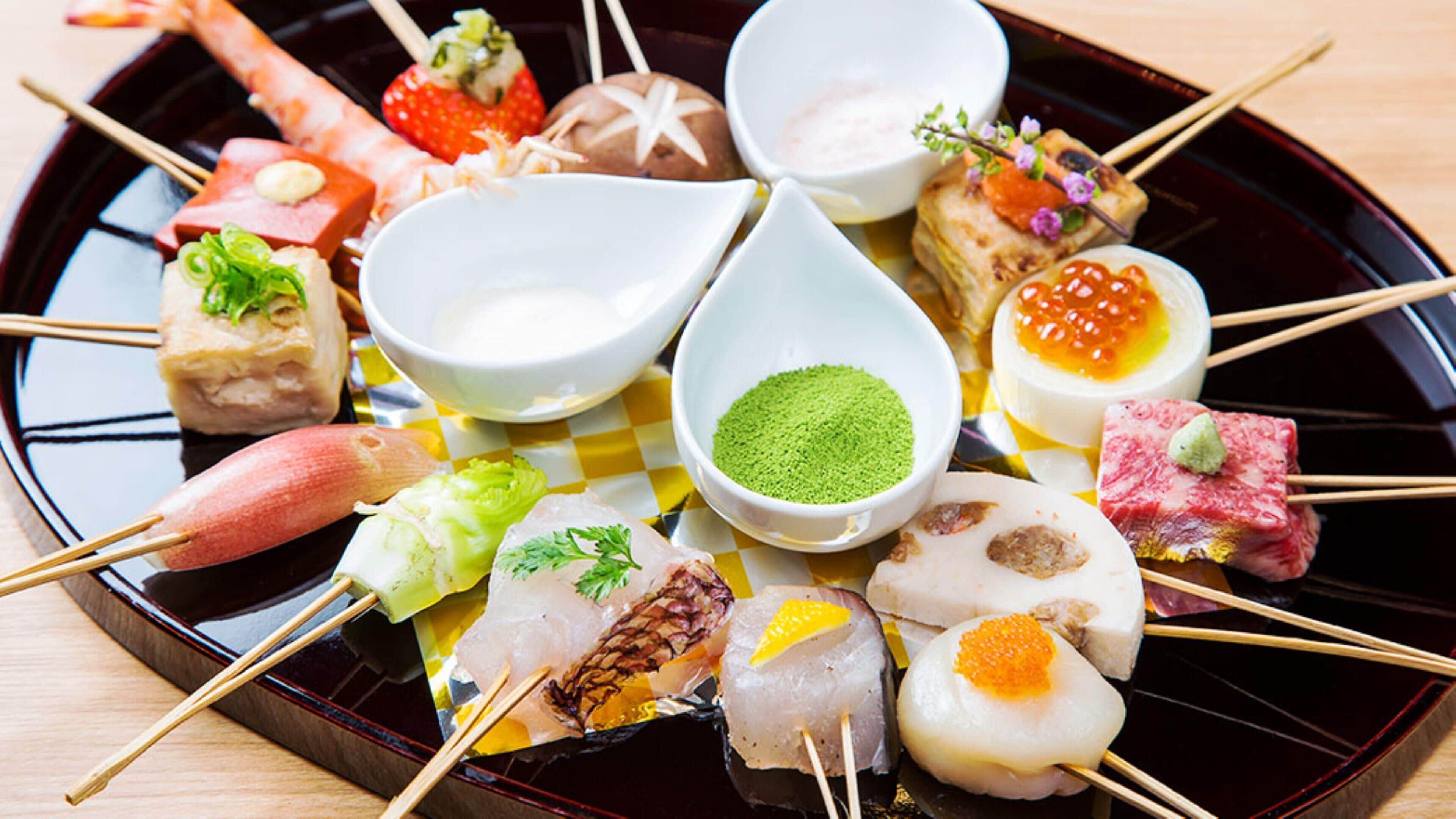 A variety of sushi and sashimi on a black plate with small white bowls of condiments.