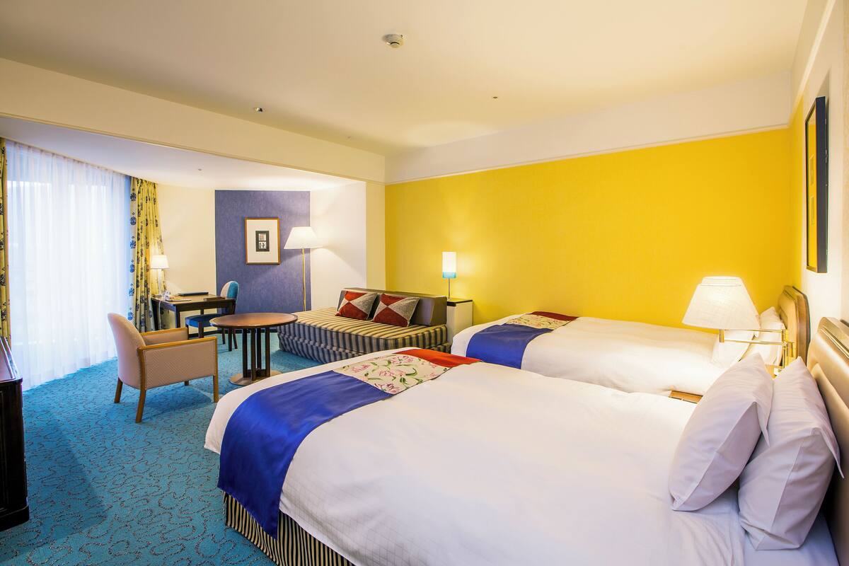 A hotel room with two beds, a desk, a chair, and a small table.