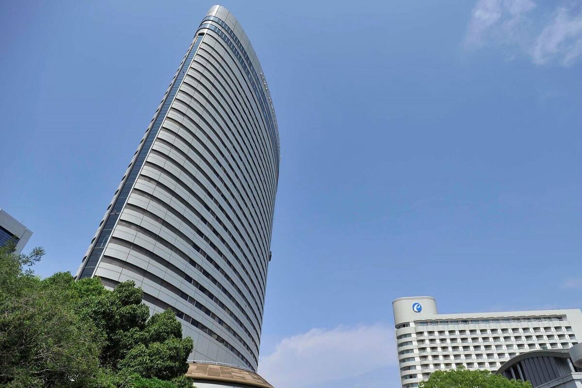 A tall, curved skyscraper with a modern design, surrounded by other buildings and trees.