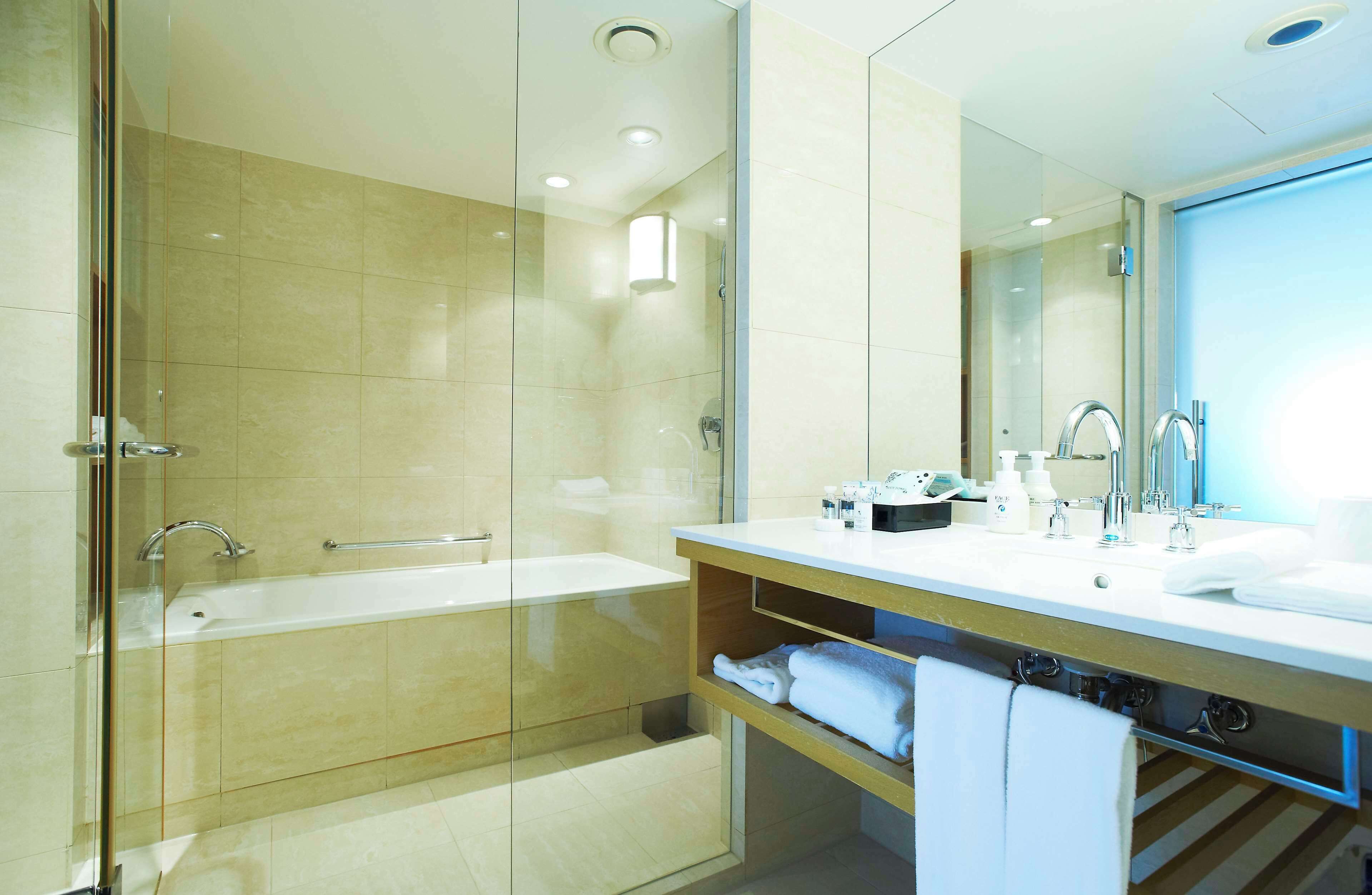 A modern bathroom with a glass-enclosed shower, a bathtub, a vanity with a mirror, and a shelf with towels.