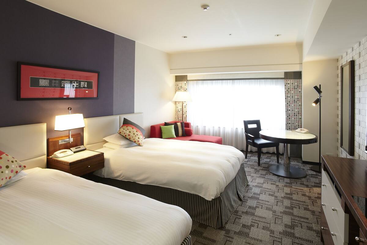 A hotel room with two beds, a desk, a chair, and a window with curtains.