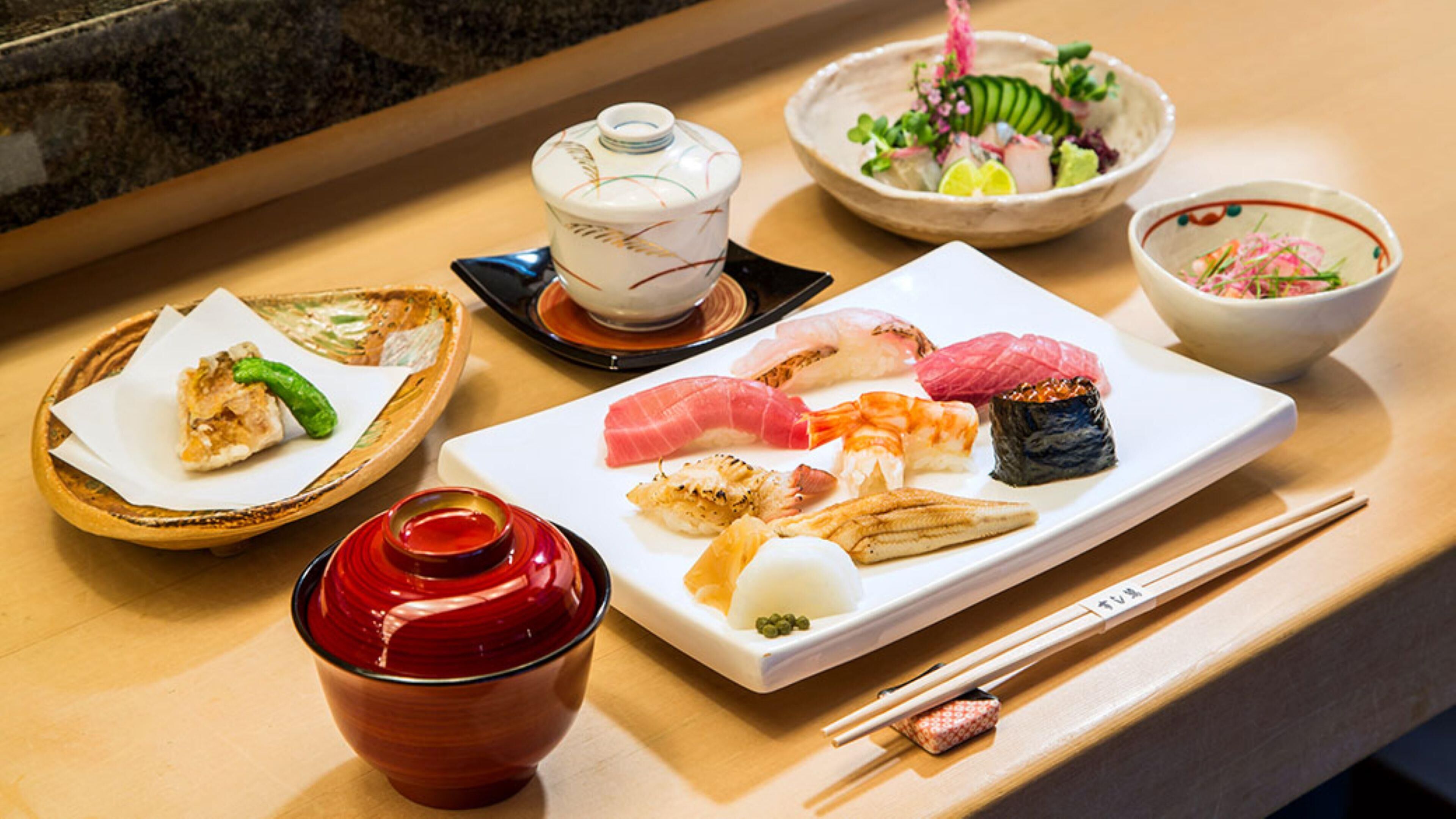 A variety of sushi dishes on a tray, a bowl of salad, a small bowl of soup, and a cup of tea on a table.
