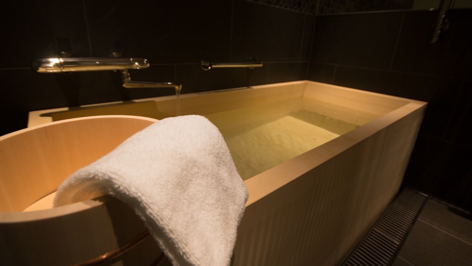 A bathtub with a white towel, a wooden chair, and a showerhead.