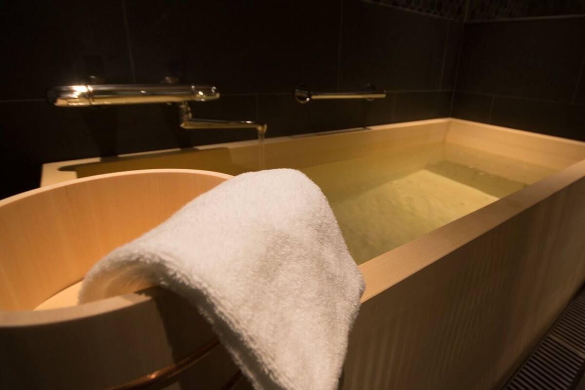 A bathtub with a white towel, a wooden chair, and a showerhead.