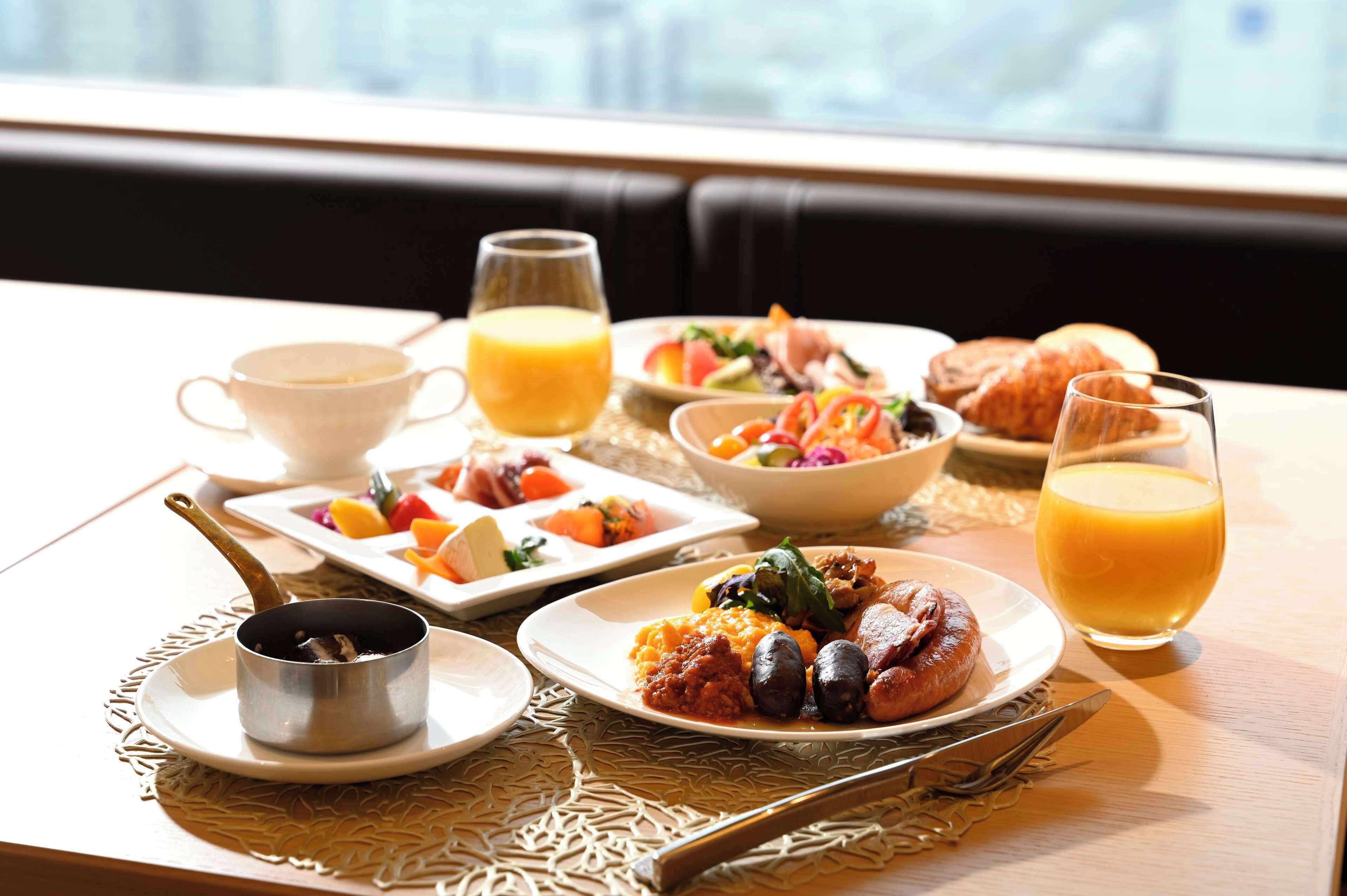 A breakfast setting with plates of food, a cup, and a glass of orange juice on a table.