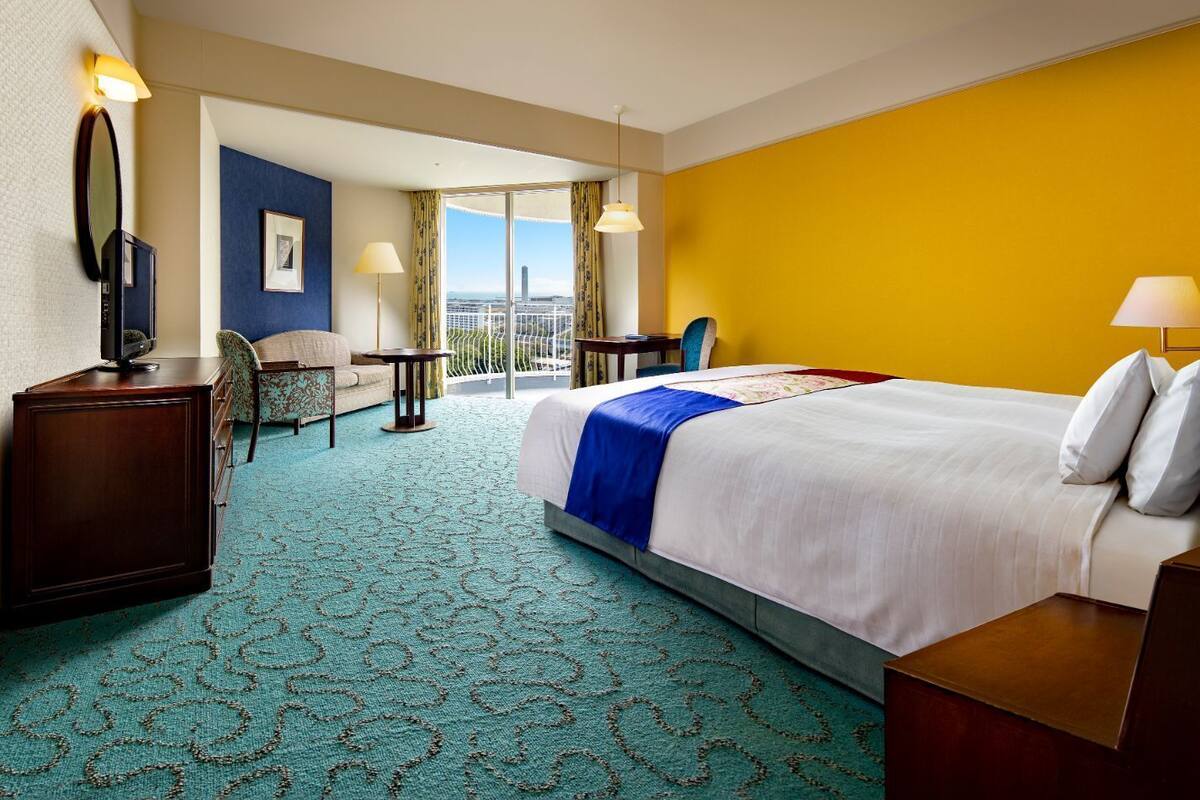 A hotel room with a bed, a desk, a chair, a TV, and a balcony with a view.