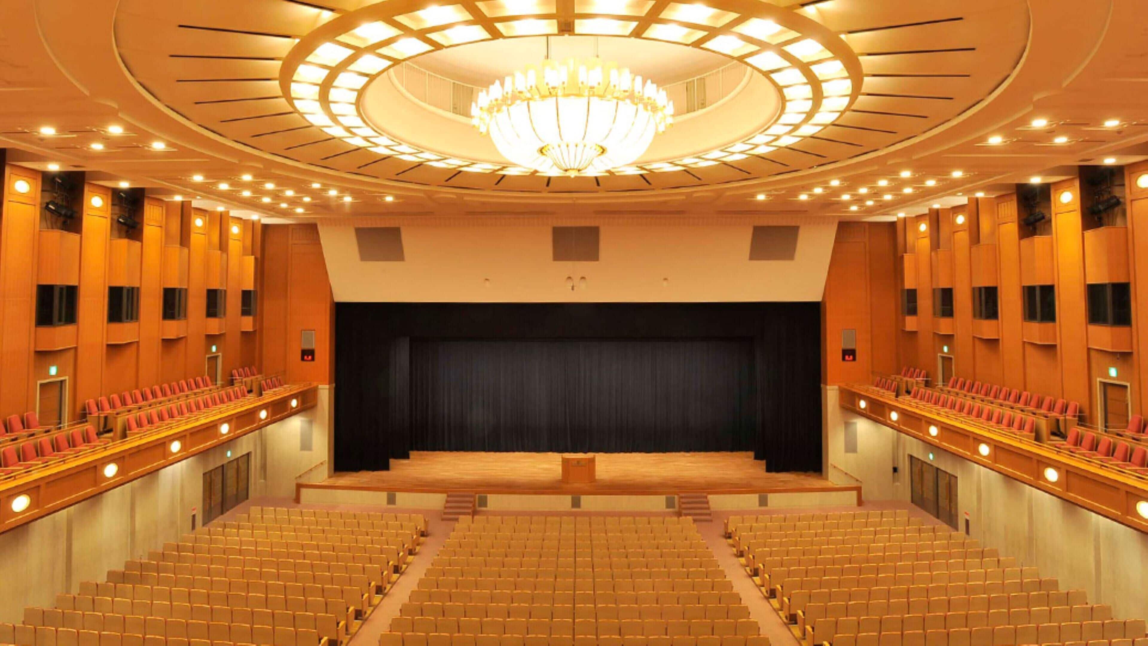 A large auditorium with tiered seating, a central stage, and a grand chandelier.