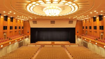 Ein großes Auditorium mit terrassenförmigen Sitzplätzen, einer zentralen Bühne und einer prächtigen Chandelier.