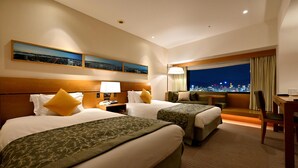 Habitación de hotel con dos camas, un escritorio, una silla y vista nocturna de la ciudad.
