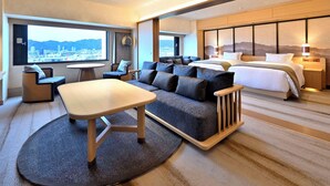 Una habitación de hotel moderna con una cama grande, un sofá, una mesa de comedor y vistas a la ciudad.