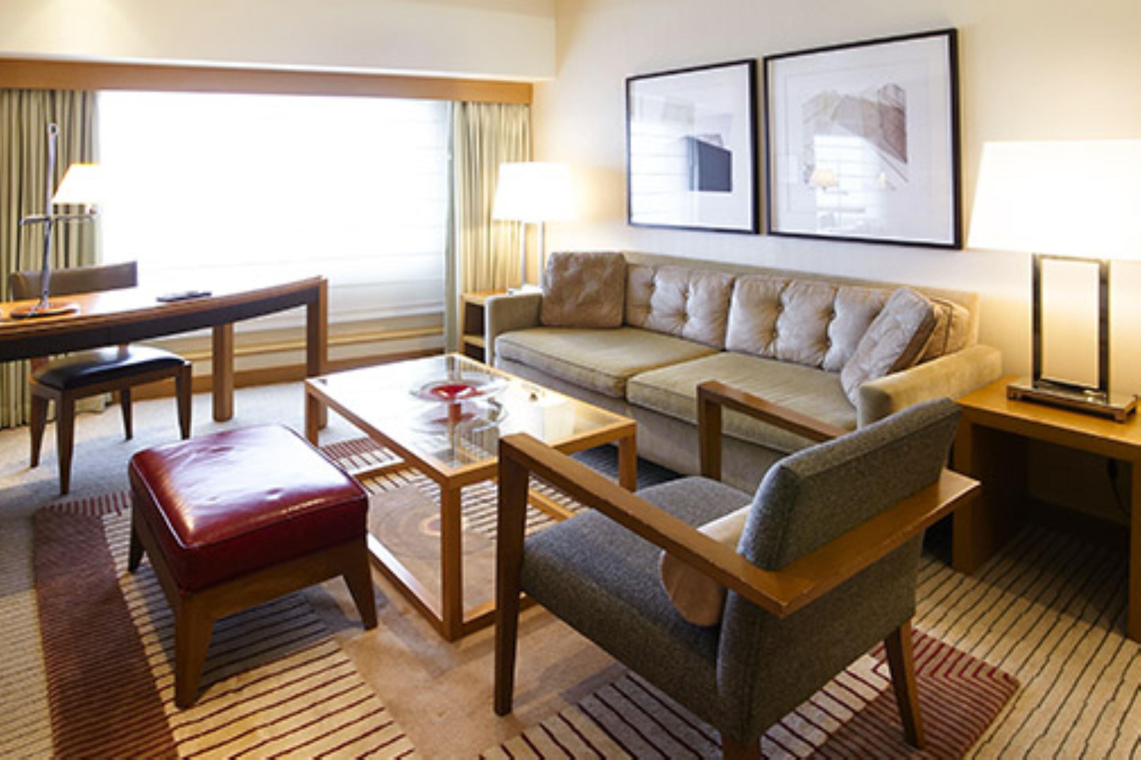Una habitación de hotel con sofá, sillón, mesa de centro y escritorio con lámpara.
