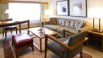 Une chambre d’hôtel équipée d’un canapé, d’un fauteuil, d’une table basse et d’un bureau avec une lampe.