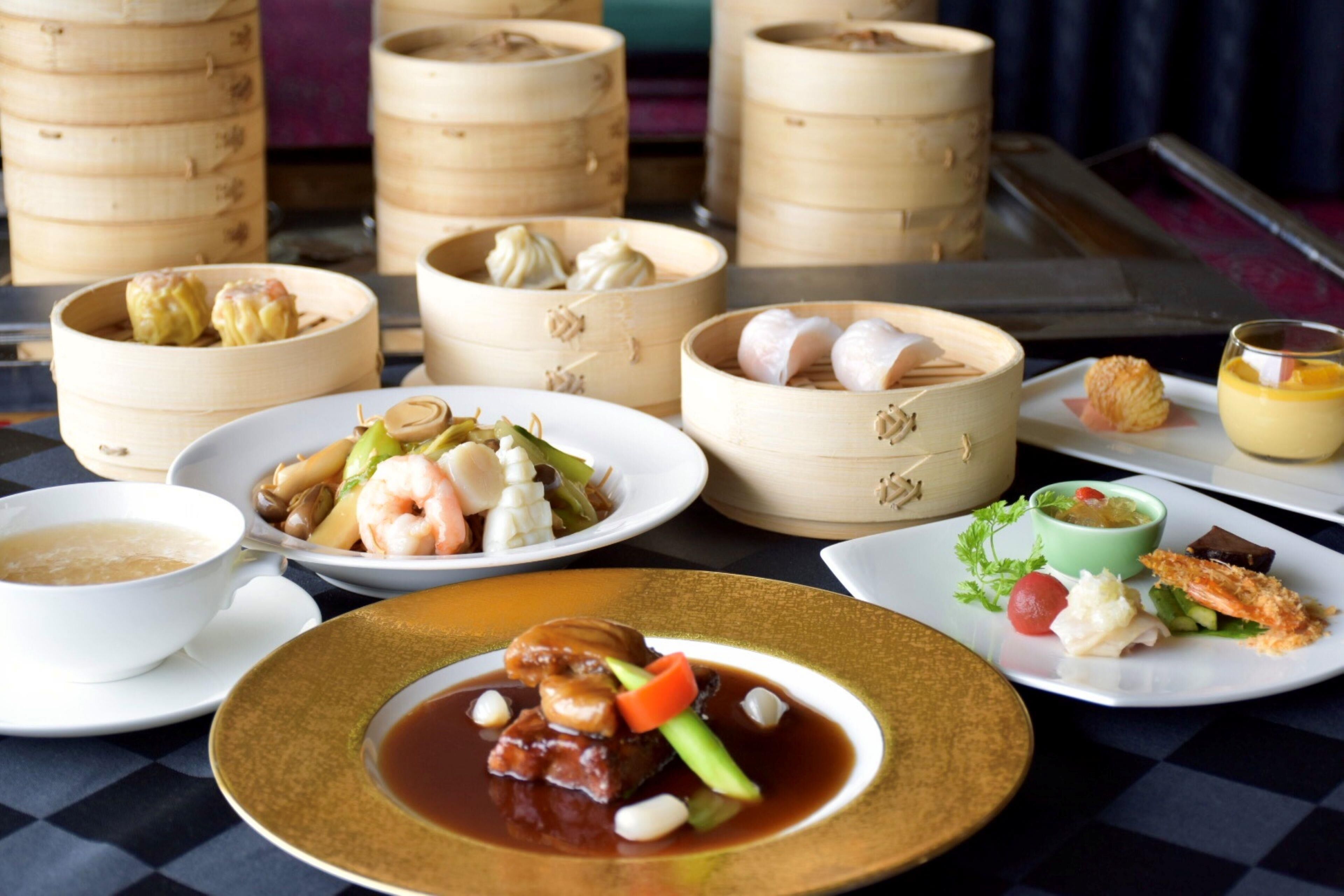 A variety of dishes on a table, including dumplings, seafood, and a bowl of soup.