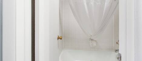 Une salle de bain blanche avec une baignoire, un rideau de douche et une serviette accrochée au mur.