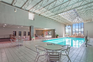 An indoor swimming pool with tiled flooring, metal chairs, and tables.