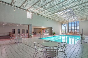 Una piscina interior con suelo de baldosas, sillas y mesas de metal.