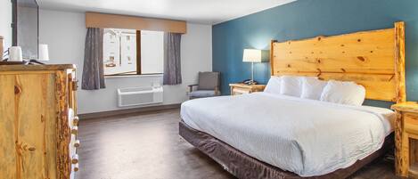 A hotel room with a large bed, a wooden headboard, a desk with a lamp, a chair, and a window with curtains.