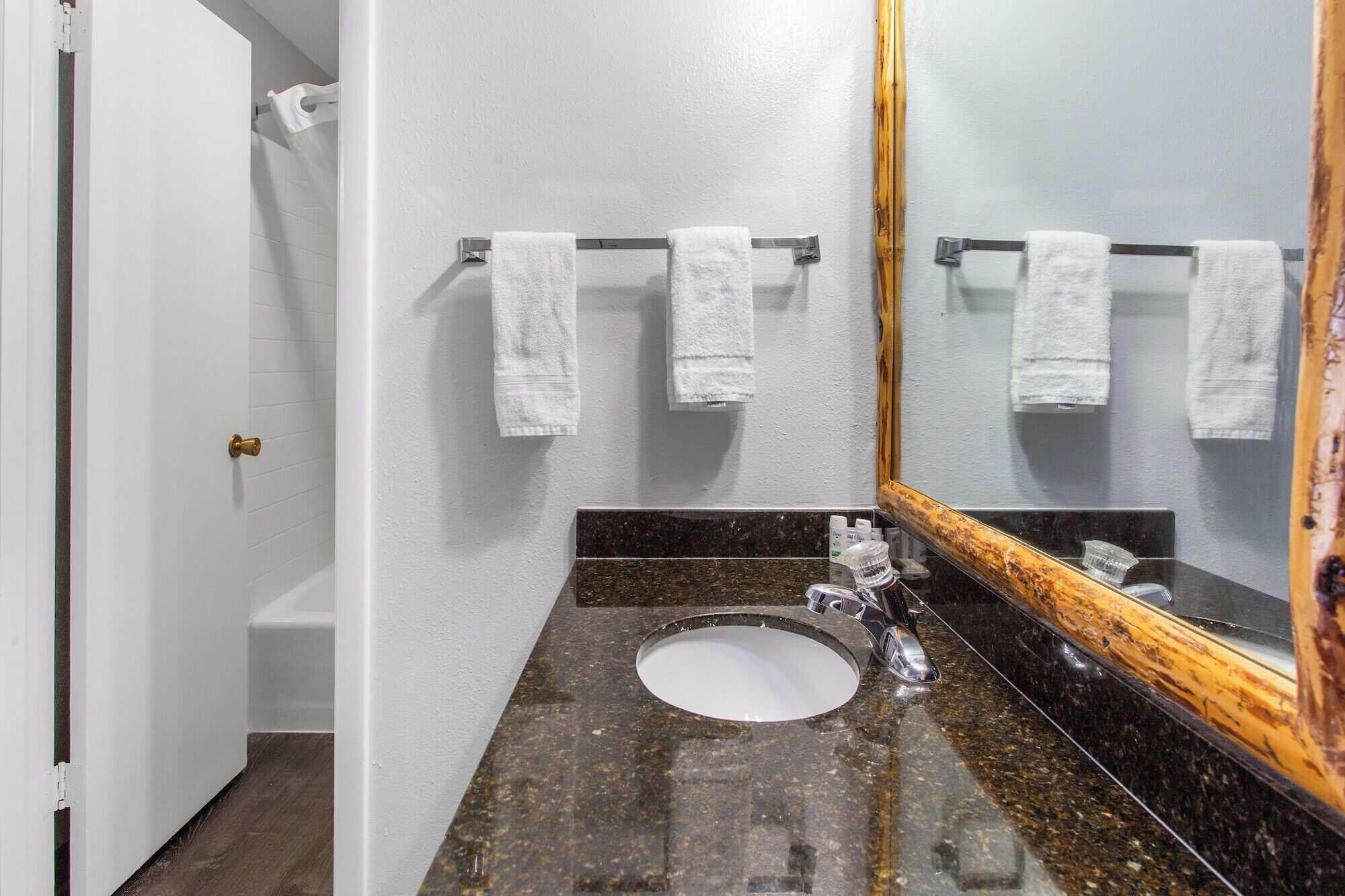Un baño con un lavamanos blanco, un espejo con marco de madera y dos toallas colgadas en un perchero metálico.