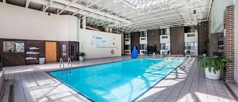 An indoor swimming pool with a tiled floor, a blue pool, and a high ceiling with metal beams.
